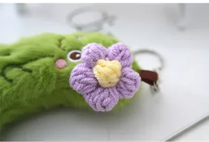 Cute green cucumber plush keychain detail shot with purple crochet flower ornament and ring.