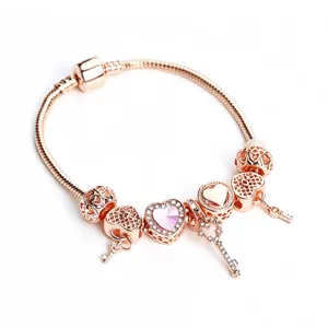 Rose gold charm bracelet detail showing intricate heart beads, dangling keys and pink crystal center.
