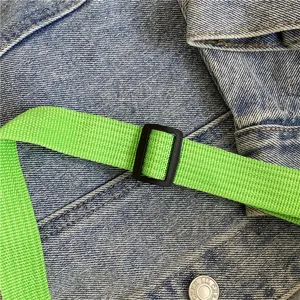 Detaillierte Nahaufnahme von Denimgewebe mit hellem gruenem Gurt und schwarzer Schnalle.