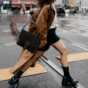 Urban street style detail view showing a black vintage crossbody messenger bag with brown buckle.