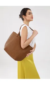 Detailed shot of a brown woven leather tote bag worn by a model in a studio setup.
