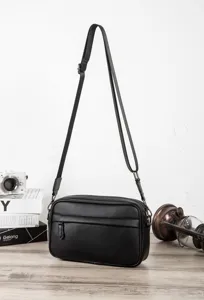 Close-up detail of black PU leather crossbody bag on wooden table with vintage props.