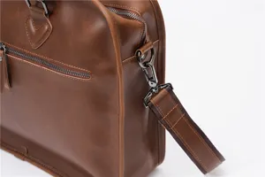 Close-up detail of retro brown PU leather briefcase with metal zippers and shoulder strap.