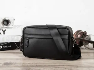 Black PU leather messenger bag detail with wide strap and zipper pocket on wood table