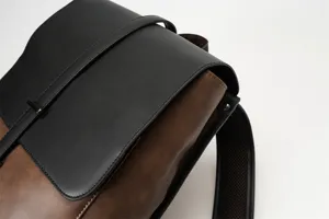 Close-up detail shot of a retro men's two-tone PU leather backpack with flap and strap.