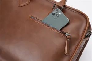 Detail shot of brown leather briefcase zipper pocket with phone slot feature. Premium texture.