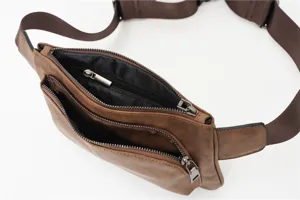 Close-up detail view of the multi-zipper brown leather fanny pack with adjustable strap.