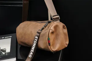 Primo piano sul cinturino della borsa a tracolla cilindrica in pelle marrone e dettagli.