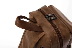 Close-up view of brown leather chest bag showing smooth zipper and sturdy top handle details.