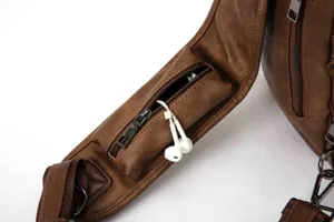 Detailed view of brown leather chest bag strap with small zipper pocket and earphone hole.