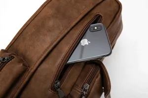 Close-up detail of brown leather chest bag zipper pocket with phone inside, durable casual style.