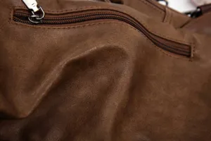 Close-up detail of men's brown leather chest bag, showing fine texture and zipper design.