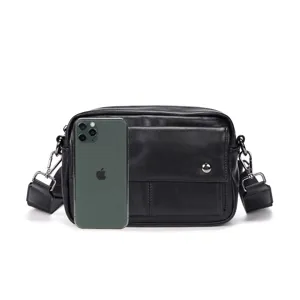 Detail view of black leather messenger bag with phone for size reference, premium style.