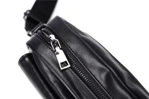 Detail shot of black leather crossbody bag featuring metal zipper and adjustable strap.