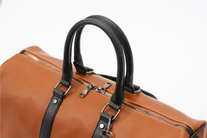 Leather travel bag detail showing sturdy black handles, smooth metal zippers, and retro brown design.