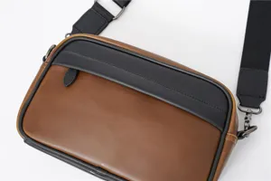 Dettaglio in primo piano della borsa a tracolla orizzontale da uomo dal design bicolore.