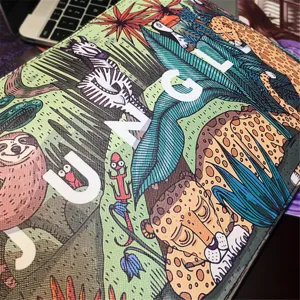 Close-up detail of jungle printed canvas clutch bag featuring vibrant animal art and letters.