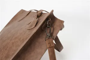 Detail shot of brown PU leather tote bag with metal hardware strap closure texture.