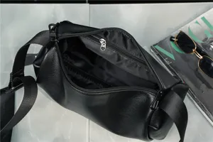 Detail view of black cylindrical crossbody bag, showing interior zipper pocket and design.