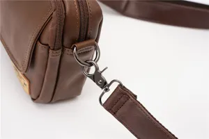 Brown leather crossbody bag detail featuring metal clasp, zipper, and adjustable strap.