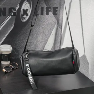 Detailed close-up of a stylish black cylinder crossbody bag on a dark desk with props.