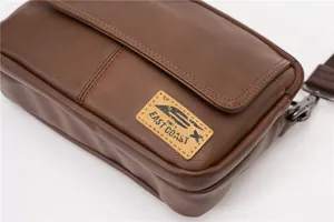 Close-up detail of a brown faux leather vintage messenger bag with shoulder strap and label tag.