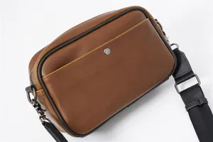 Primo piano sulla struttura in pelle marrone, minuteria metallica e tracolla resistente di borsa.