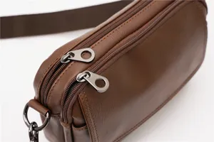 Close-up detail of brown leather messenger bag metal dual zippers pull tabs and hardware.