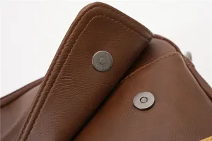 Brown leather messenger bag detail snap button texture close up stylish retro accessory.