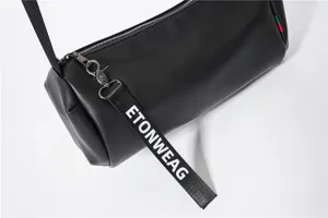 Black leather cylindrical crossbody bag featuring a stylish branded strap detail closeup view.