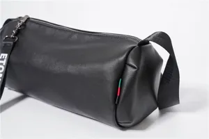 Close-up detail of black leather cylinder barrel cross-body shoulder bag with strap.