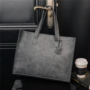Grey PU leather tote bag detail hanging on door handle, stylish minimalist design handbag.
