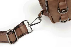 Close-up detail showing the sturdy metal hardware and adjustable strap of the brown leather chest bag.
