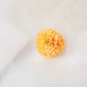 Detailed close-up of a yellow artificial flower hair clip, fluffy floral design, soft tulle backdrop.