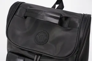 Close-up detail of black travel backpack showing top handle and circular brand badge.