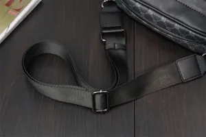 Close-up of black canvas crossbody bag strap and monogram pattern detail on dark wood.