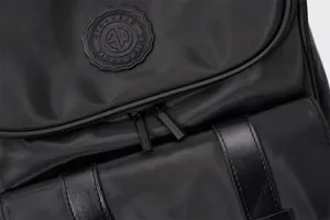Black fashion backpack detail shot, showing textured fabric, brand logo patch and zippers.