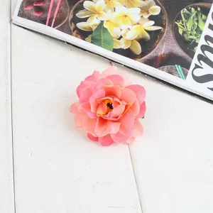 Close-up van een stoffen bloemenhaarspeld met roze verloop op een witte houten achtergrond.
