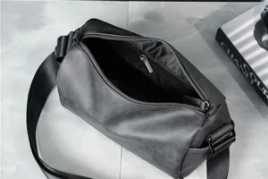 Close-up detail shot of black cylindrical shoulder bag with zipper and wide strap.