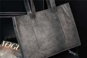 Detail view of grey PU leather tote bag, showing fine texture, dual handles and zipper.