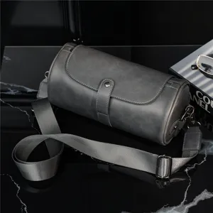 Detailed view of dark grey cylindrical crossbody bag, adjustable strap and metal hardware.