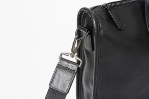 Vista dettagliata della minuteria della borsa uomo nera, fibbia metallica e tracolla.