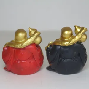 Detailed view of two miniature laughing Buddha monk figurines in red and black robes carrying gold bags.