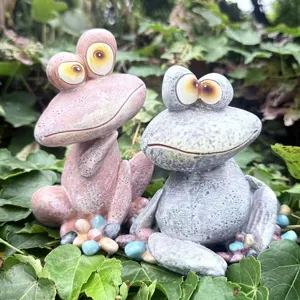 Closeup view of quirky resin frog figurines set among green leaves, ideal for garden decor.
