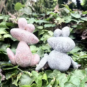 Close-up of cute quirky pebble frog resin garden ornaments displayed in green leaves.