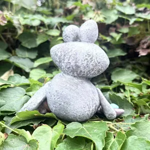Detail shot of a grey resin frog figurine placed among green leaves, perfect outdoor decor.