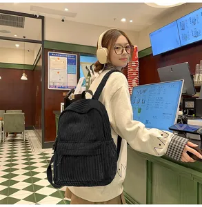 Detailed view of women's black corduroy backpack worn by model in a cafe setting.