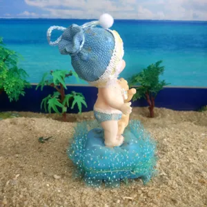 Resin baby doll holding a bear toy, standing on a blue cushion for sandplay therapy and display.