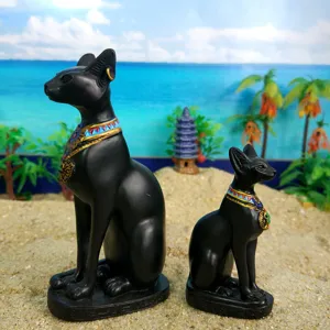 Detailed view of black resin Bastet cat statues with colorful collars on sand background.