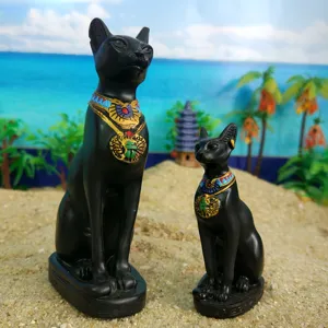 Detail shot of black Egyptian Bastet cat resin figurines with colorful collars on sand backdrop.